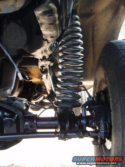 Underside view of a vehicle's front suspension with a large coil spring and differential