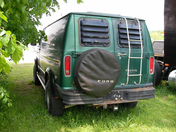 Rear view of a green 1978 Ford E250 van with a spare tire on the back and a ladder on the side