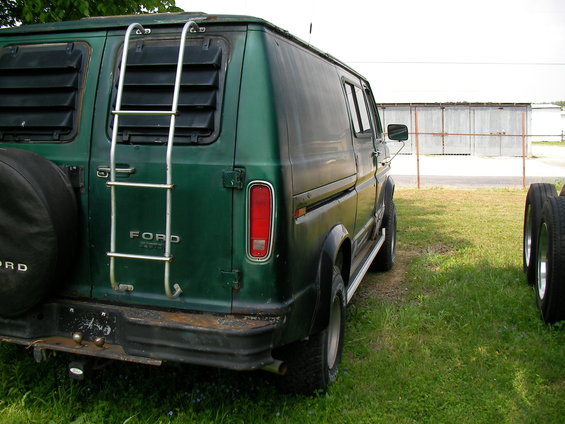 Rear view of a green 1978 Ford E250 van with a ladder on the back and louvers on the windows