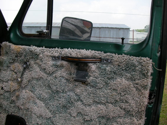 Green vehicle door panel with fuzzy gray carpet and a chrome window crank