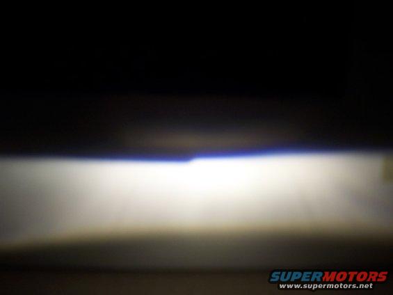 car headlight beam shining forward, supermotors.net logo visible
