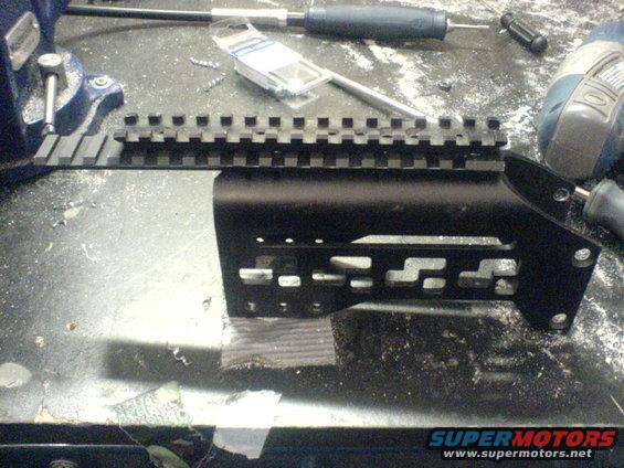 Black metal gun accessory rail with Picatinny slots on a workbench