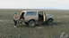 1990 Ford Bronco - A tan 1990 Ford Bronco is parked in an open field with its doors open and a spare tire carrier mounted on the rear.