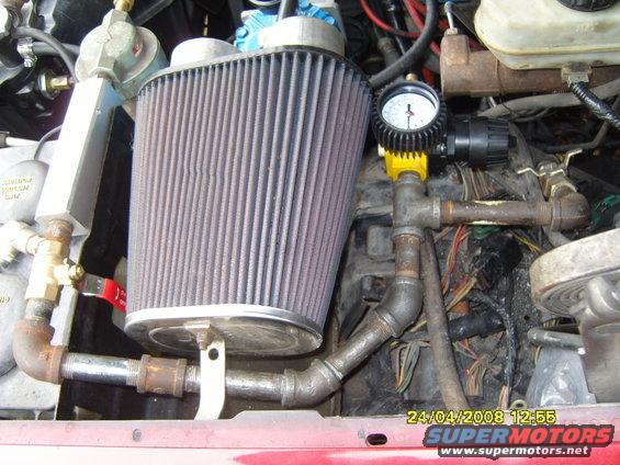 Aftermarket air filter and plumbing with a pressure gauge installed in an engine bay