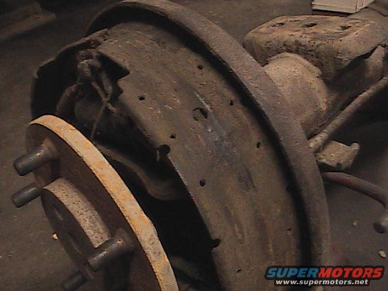 Close-up of a rusty rear drum brake assembly with a wheel hub and studs