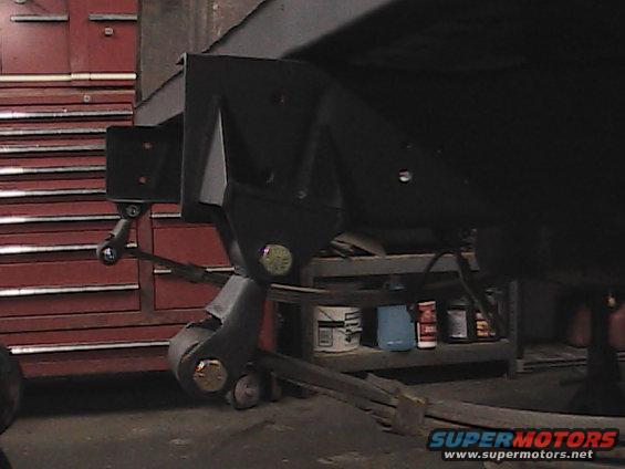 Close-up of vehicle frame and leaf spring suspension in a garage, with a red toolbox in the background