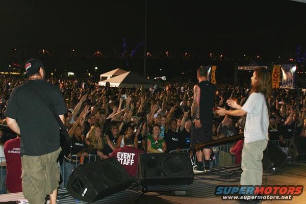 Concert crowd with performers on stage at night, bridge in background
