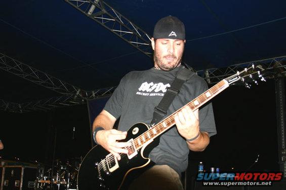 Man in AC/DC shirt playing black electric guitar on stage