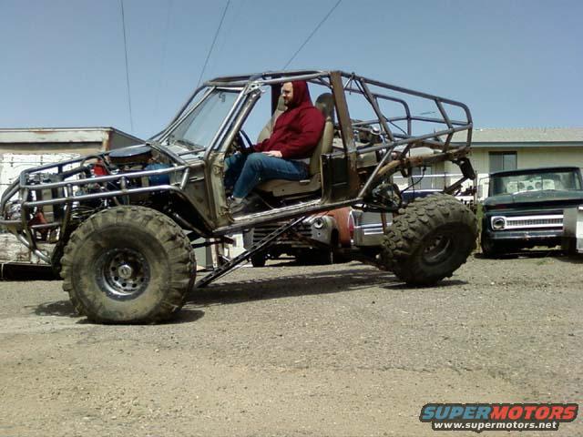 Custom buggy with roll cage and large tires, driver visible. Another truck in background