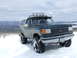 1988 Ford Bronco - A lifted Ford Bronco sits in a snowy landscape under a cloudy sky.