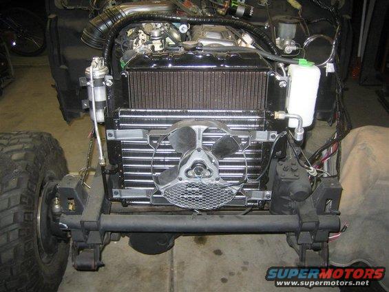 Front view of a vehicle's engine bay, showing the radiator, fan, and some engine components. The vehicle is partially disassembled