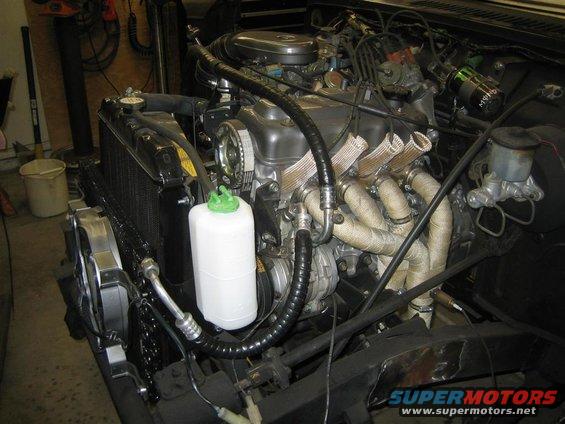 1987 Suzuki Samurai engine bay with exhaust manifold wrapped in heat tape, radiator, and coolant reservoir
