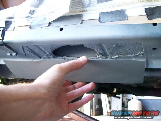 Hand holding a piece of metal against a rusted car undercarriage with visible hole