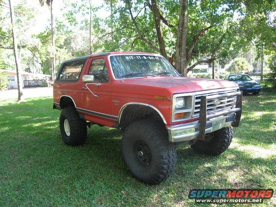 Red Ford Bronco with lifted suspension and large tires parked on grass