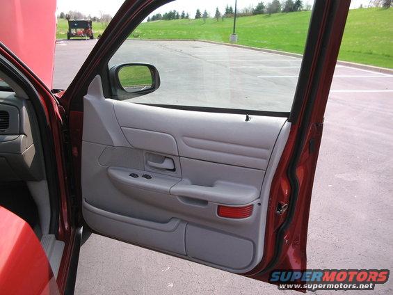 Red car's interior driver's side door panel with gray trim, power window controls, and a red reflector. Hood is open