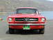 1965 Ford Mustang - A classic red 1965 Ford Mustang is shown from the front, parked near a body of water with mountains in the background.