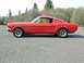 1965 Ford Mustang - A red 1965 Ford Mustang coupe is shown from the side, parked outdoors on an asphalt surface.