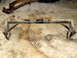 1996 Ford Bronco - A black metal suspension crossmember with welded brackets and leaf springs is shown on a concrete floor.