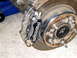 1996 Ford Bronco - Close-up of a black Wilwood brake caliper mounted on a rusty rotor and hub assembly.