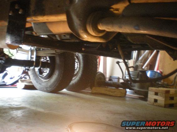 Undercarriage view of a vehicle's rear axle and dual wheels, supported by wooden blocks