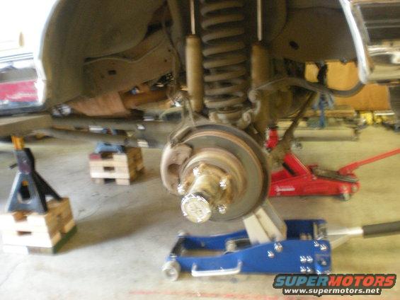 Front suspension of a vehicle on jack stands, showing coil spring, shock absorber, brake rotor, and wheel hub