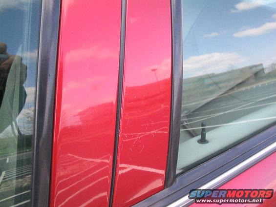 Red car door with visible scratches and a reflection of the sky and clouds in the window