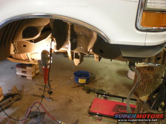 vehicle frame with suspension components visible, jack stands and tools on the floor