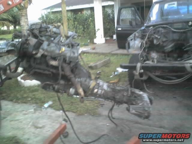 Engine and transmission removed from a black truck, with the truck's front end visible