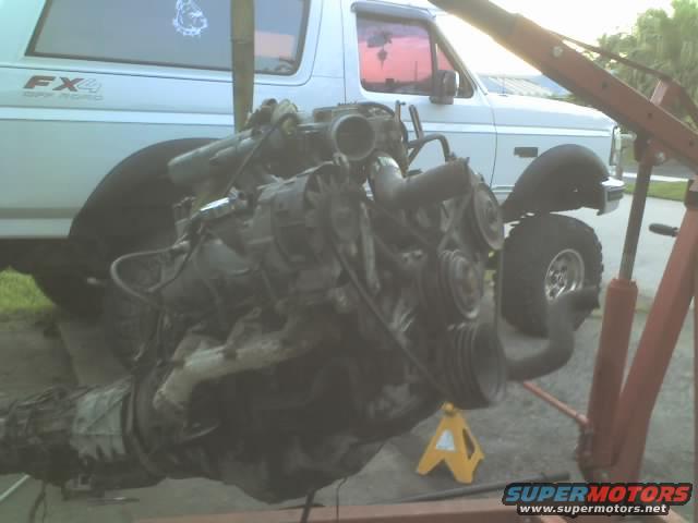 Engine on an engine hoist, with a Ford Bronco in the background