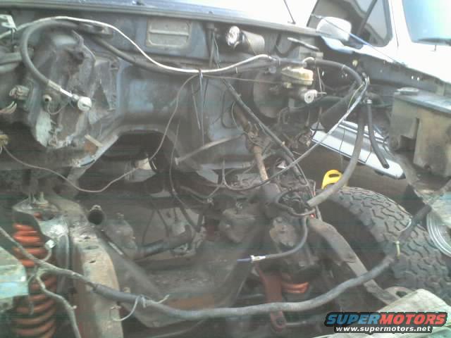 vehicle engine bay with exposed wires and hoses, tire visible