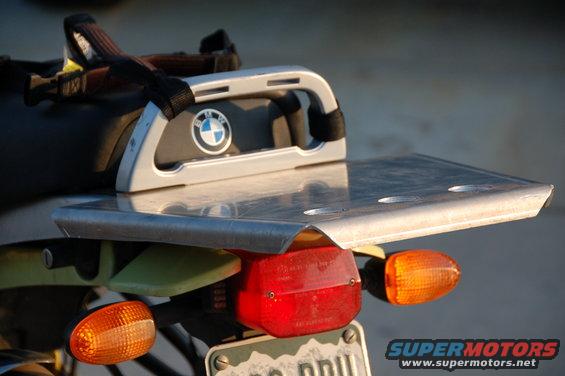 Motorcycle rear rack with BMW logo and metal plate. Red taillight and orange turn signals visible