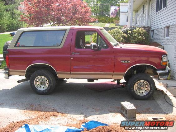 Red Ford Bronco with tan top, side view, spare tire on rear door