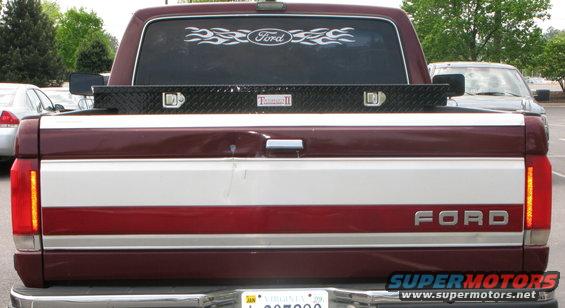 Rear of a 1991 Ford F-150 pickup truck with a toolbox in the bed and a Ford flame decal on the rear window