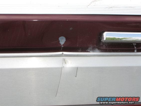 Maroon and silver truck bumper with dent and paint chip. Chrome trim visible