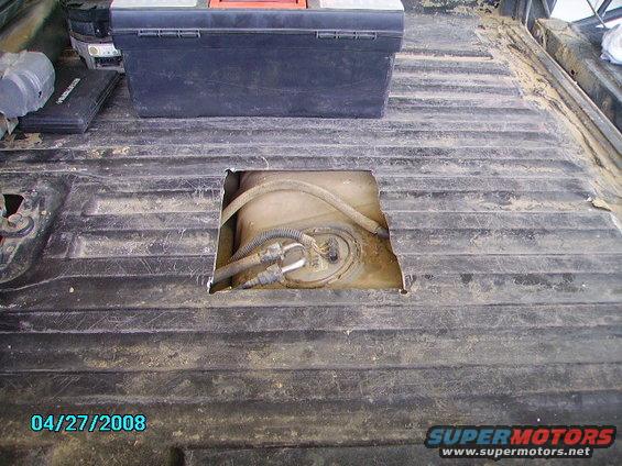 Truck bed with a square hole revealing the fuel tank and lines. Toolbox and other items are in the background
