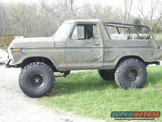 Olive green 1978 Ford Bronco with large off-road tires and a roll cage, seen from the side