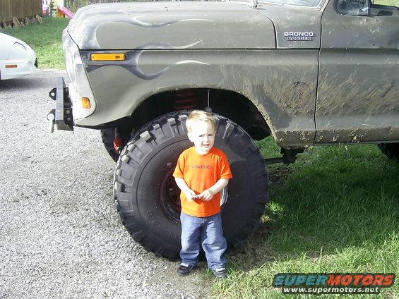 Green 1978 Ford Bronco with flames and oversized tires, child for scale