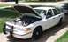 1996 Ford Crown Victoria - A white 1996 Ford Crown Victoria is parked on a driveway with its hood open, revealing the engine compartment.