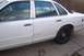 1996 Ford Crown Victoria - The side of a white sedan shows damage along the lower body trim and a black steel wheel.