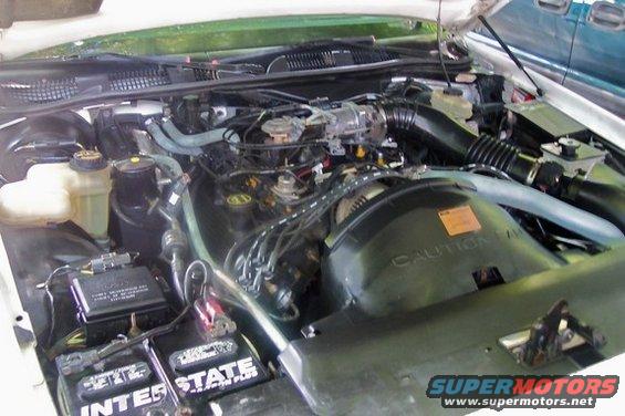 Engine bay with visible batteries and hoses. Caution label on fan shroud