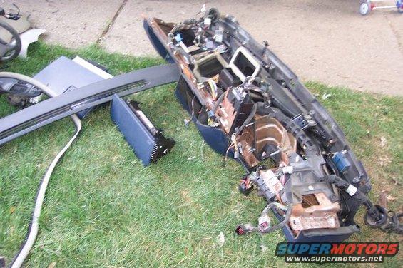 Disassembled car dashboard with exposed wiring and components lying on grass
