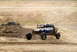 2008 Ford Bronco - An off-road buggy jumps over a dirt mound, with another vehicle partially buried in the dirt in the background.