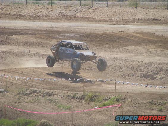 Blue off-road buggy airborne over dirt track, side view