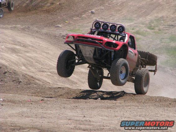Red off-road truck airborne over dirt track, front wheels off ground