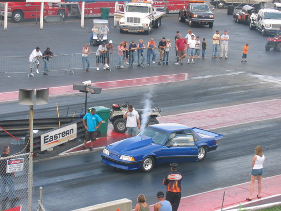 Blue Ford Mustang drag car with a hood scoop on a race track, emitting smoke