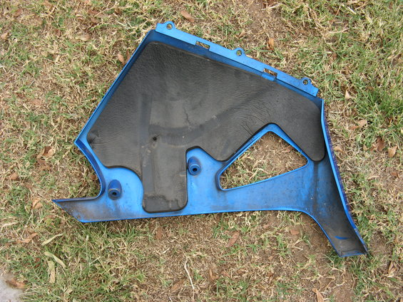 Blue motorcycle fairing part with black textured insert, lying on grass