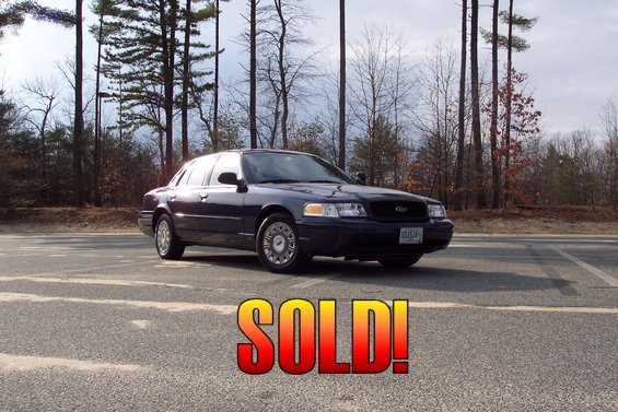 Dark blue 2001 Ford Crown Victoria parked on asphalt with trees in background