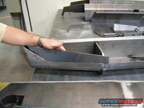 Hand holding a metal bumper section on a workbench with other metal parts