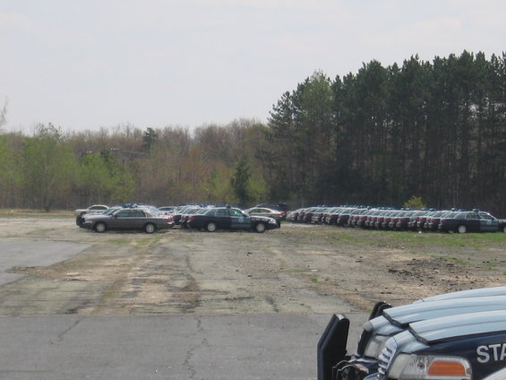 Fleet of 2001 Ford Crown Victoria police cars parked in a lot with trees in the background