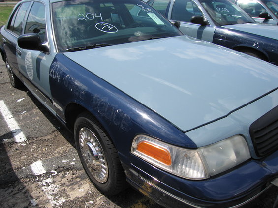 Blue and light blue 2001 Ford Crown Victoria police car, front passenger side view, showing damage on fender